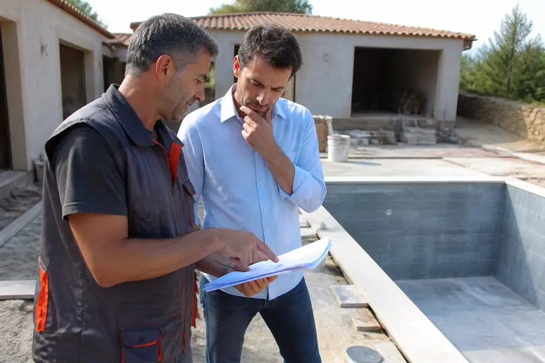 Un propriétaire discute avec un carreleur du coût du carrelage pour sa future piscine, évaluant l'investissement pour un revêtement de qualité.