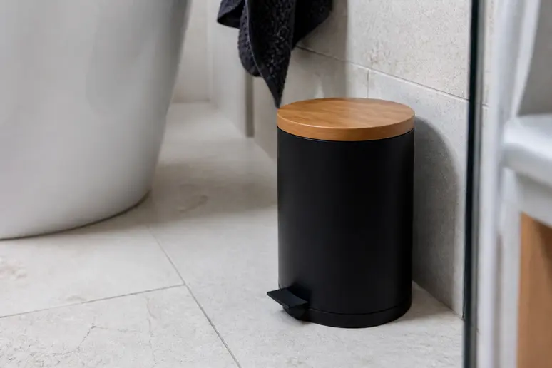 Gros plan sur une poubelle de salle de bain noire mate en acier inoxydable avec un couvercle en bois, bien intégrée dans une décoration intérieure.