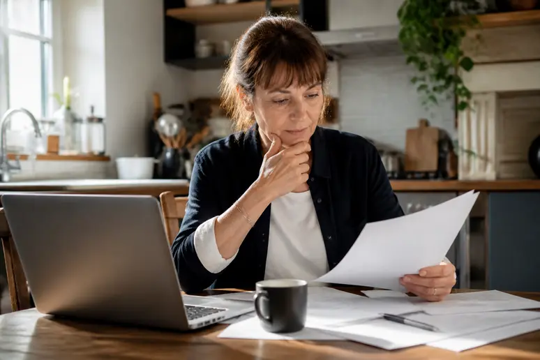 Femme examinant des documents et un ordinateur portable à table, recherchant des aides financières pour l'installation d'une pompe à chaleur.