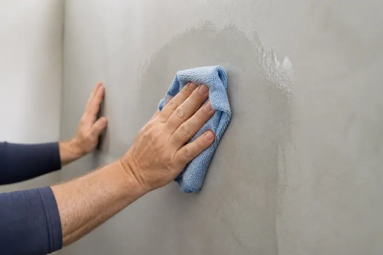 Mains nettoyant soigneusement un mur pour le préparer à la pose de revêtements adhésifs.