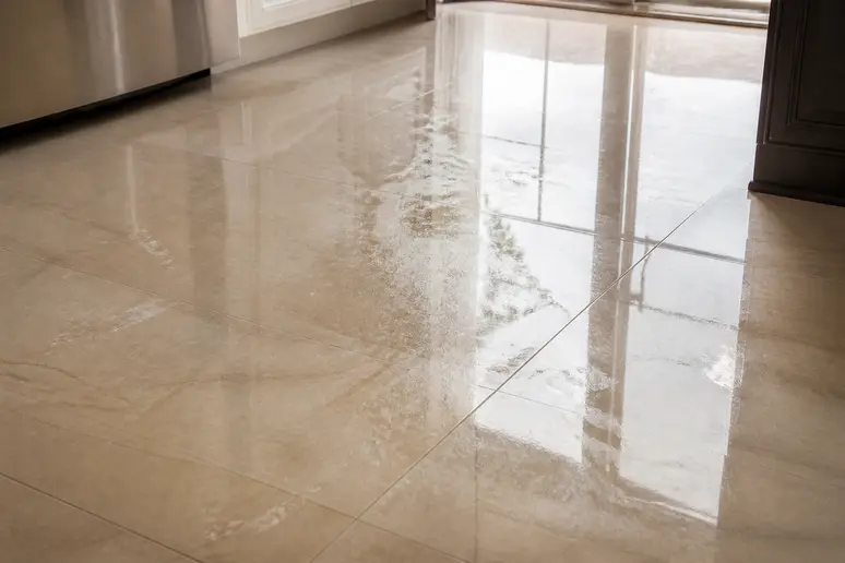 Surface de carrelage beige brillant révélant des traces de pas et des gouttes d'eau séchées.