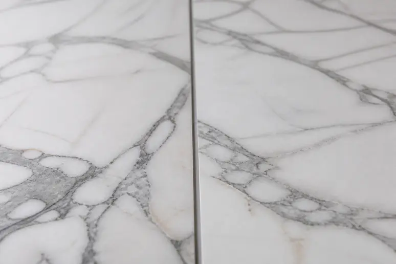 Gros plan comparatif de deux surfaces : marbre naturel aux veines profondes et grès cérame imitation marbre parfaitement rendu.