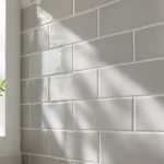 Pose de carrelage mural cuisine gris clair, mis en valeur par la lumière naturelle traversant une fenêtre.