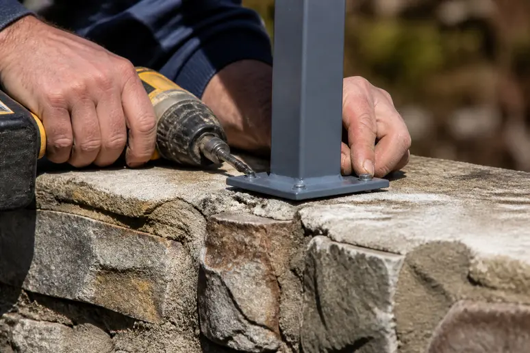 Mains d'un artisan fixant un support métallique de poteau sur le sommet d'un muret.