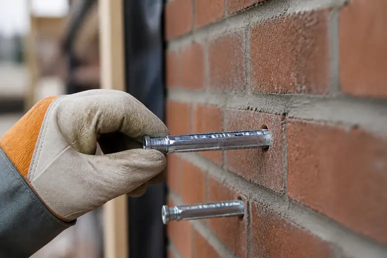 Mains d'un bricoleur insérant des chevilles dans un mur en briques pour fixer un meuble.