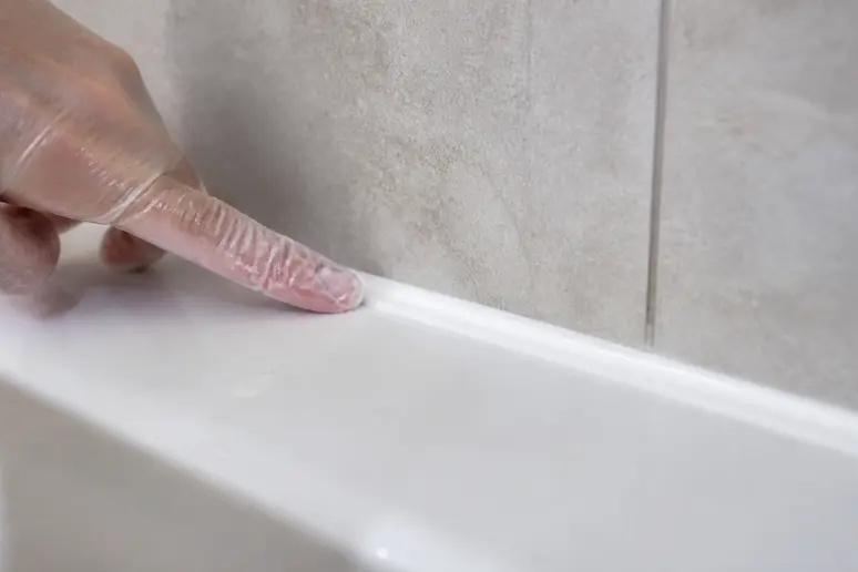 Application et lissage d'un cordon de silicone blanc avec un doigt humidifié.