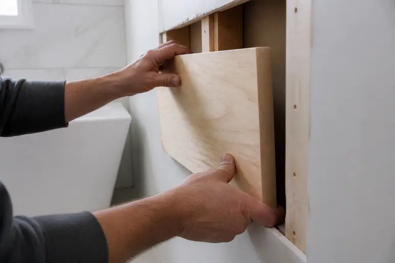 Mains installant un panneau de bois de renfort derrière une cloison en plaque de plâtre.