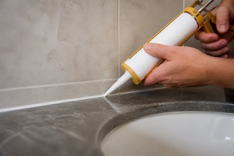 Application précise de silicone sanitaire sur le bord d'un plan vasque dans une salle de bain.