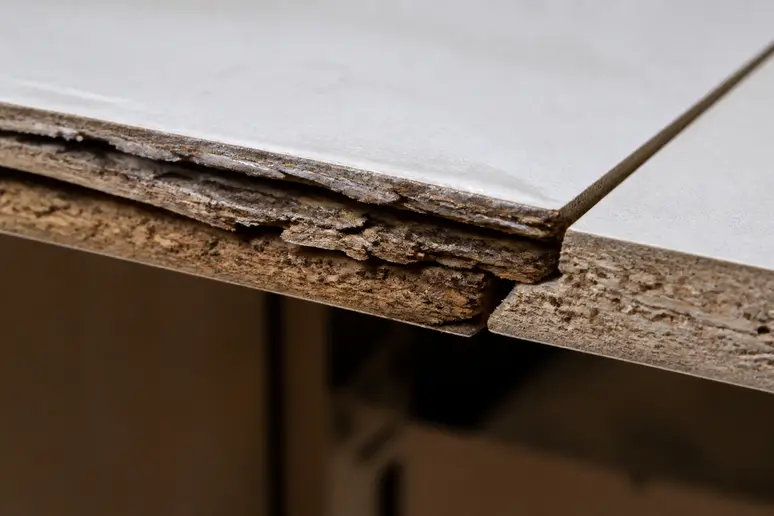 Gros plan sur le bord dégradé d'un meuble en MDF présentant un gonflement dû à l'humidité.