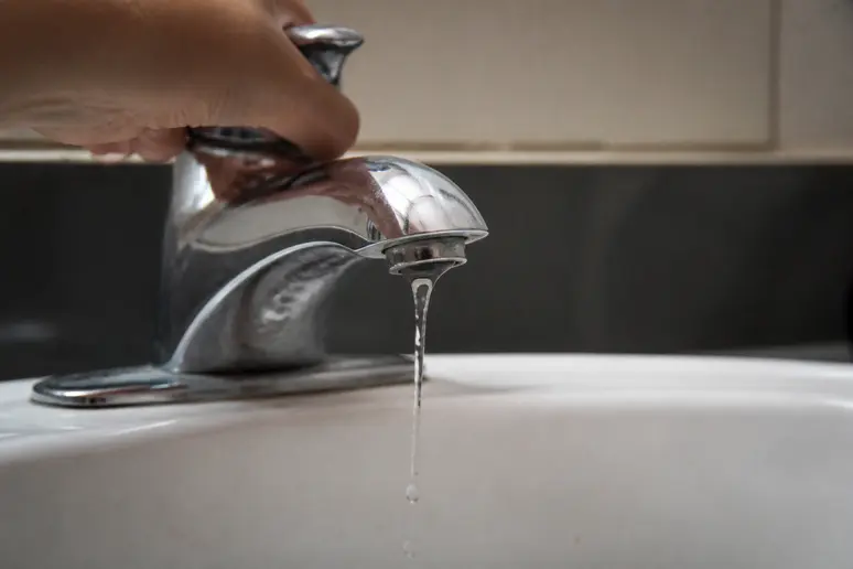 Gros plan sur un filet d'eau tiède tombant d'un robinet de salle de bain, soulignant un débit faible.