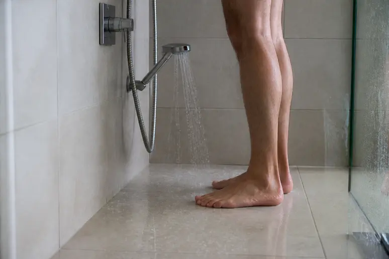 Pieds sous une douche à l'effet pluie produisant un filet d'eau très faible, signe d'un débit insuffisant.