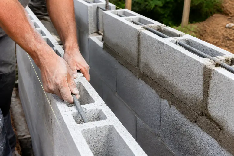 Mains d'un maçon insérant des fers dans un bloc à bancher, comparé à des blocs creux avec chaînage.