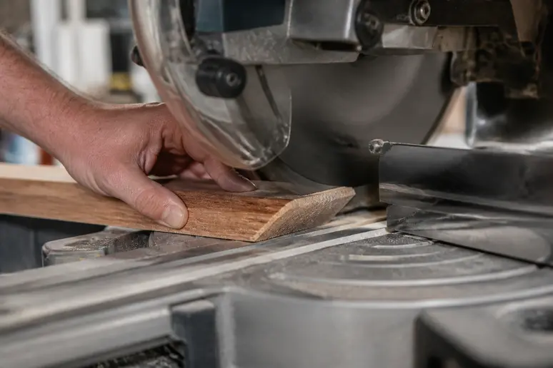 Mains habiles coupant une lame de parquet en bois selon un angle précis de 45 degrés.