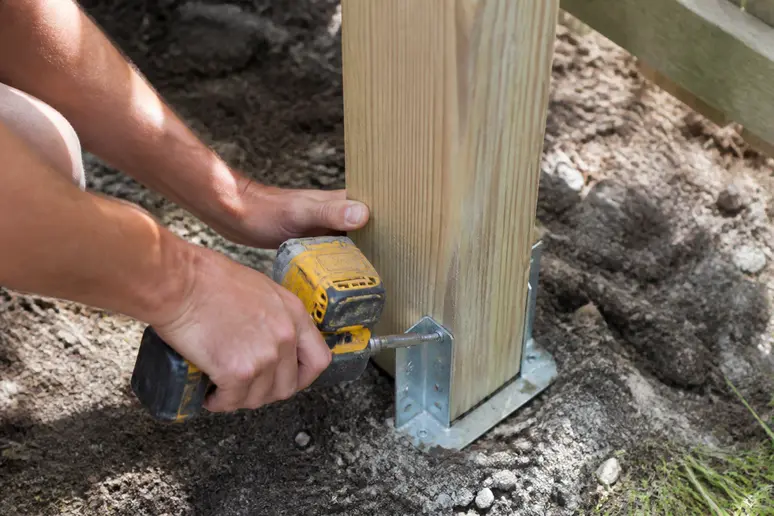 Installation d'un support métallique au pied d'un poteau pour le choix de panneaux de clôture en bois
